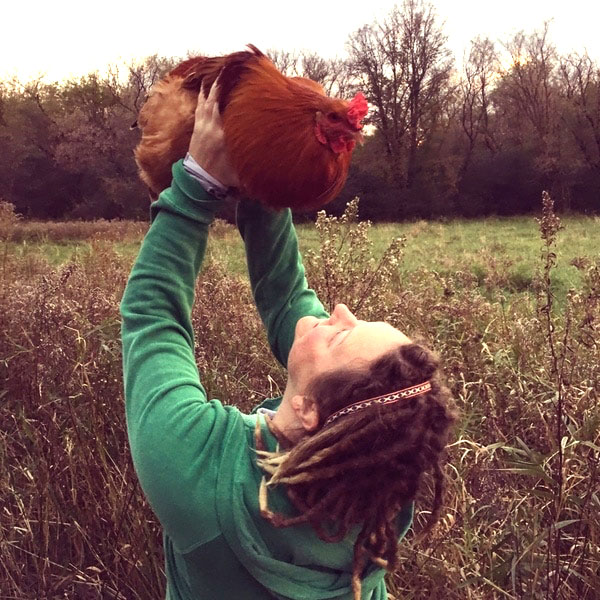 Woman looking up at a chicken she is holding above her head.
